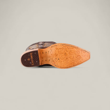 The image shows the sole of the Susan Brown - Tall Shaft - Snip Toe womens boot. The brown leather sole features intricate floral and scrollwork patterns, with LUCCHESE and a star printed on the heel, set against a light gray background.
