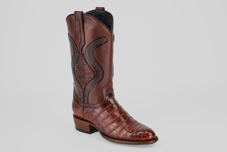 The James Platimun - Dark Cogñac - Roper Toe (Diamond) is a single men's brown leather western boot, featuring a pointed toe, alligator-patterned foot, decorative shaft stitching, and a low stacked heel on a light gray background.