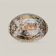 The Oval Rose Gold Cattle Cross Buckle is adorned with alpaca silver and gold, featuring intricate floral and geometric engravings and a central motif of a cross with cattle against a light gray background, inspired by classic western designs.