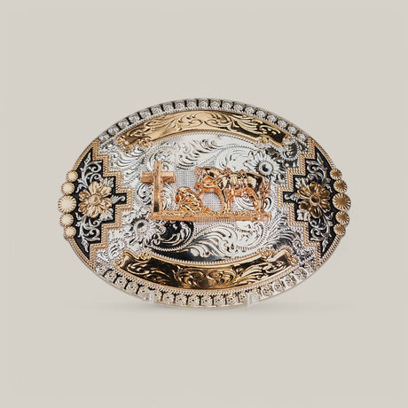 The Oval Rose Gold Cattle Cross Buckle is adorned with alpaca silver and gold, featuring intricate floral and geometric engravings and a central motif of a cross with cattle against a light gray background, inspired by classic western designs.