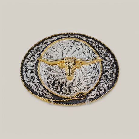 The Oval Gold Longhorn Buckle features an ornate design with a golden longhorn skull embossed at the center, surrounded by intricate alpaca silver filigree patterns on a contrasting dark background.