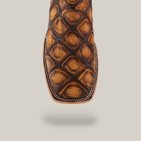Close-up of the toe on the Big Bass Pirarucu Print Rustic Honey - Square Toe boot, highlighting its textured, scale-like pattern and decorative stitching along the edge against a plain light background.