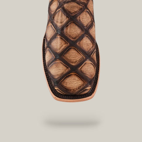 Close-up of the square toe of the Big Bass Pirarucu Print Rustic Camel cowboy boot, featuring an intricate diamond-patterned design on brown leather, shown against a plain light beige background.