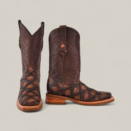A pair of Big Bass Pirarucu Print Rustic Brown - Rodeo Toe boots, crafted from dark leather with lighter brown accents, are displayed on a plain light background—one facing forward, the other turned to the right.