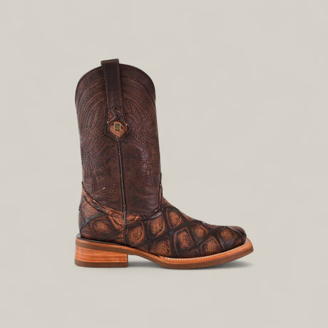 The Big Bass Pirarucu Print Rustic Brown - Rodeo Toe boot features a rustic brown finish, textured scale-like pattern on the lower part, detailed stitching on the shaft, and is displayed against a light beige background.