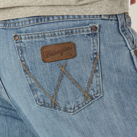 A detailed image shows the back pocket of Mens Wrangler Retro Relaxed Fit Bootcut Jean - WRT20CR in light blue, featuring brown stitching and a leather patch with the brand name. Above the jeans, there is a partially visible gray shirt.