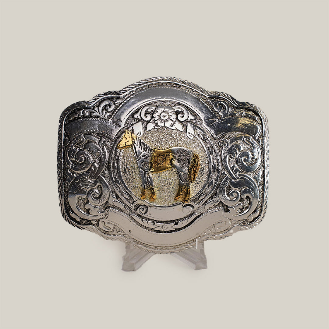 The Floral Full Horse Buckle is a decorative Texas-style buckle made from alpaca silver. It showcases an engraved gold horse at the center, surrounded by ornate western designs and floral motifs, making it a standout accessory.