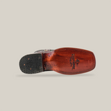 The image highlights the sole of the Exotic Caiman Hornback - Black Cherry - Rodeo Toe boot. Crafted with precision, it features a wooden sole with a brand logo and Handcrafted stamp, plus a textured rubber heel. Set against a plain white backdrop, this piece blends craftsmanship with tradition.