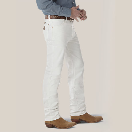 Wearing a blue shirt tucked into Wrangler Cowboy Cut Slim Fit Jeans in white (0936WHI), accessorized with a patterned belt and brown cowboy boots, the person is shown from the waist down against a plain background, highlighting the essence of Cowboy Cut style.