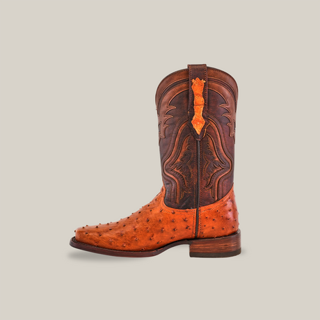The Exotic Ostrich - Brandy boot features remarkable craftsmanship with a brown upper adorned with intricate stitching and an orange textured lower. Made likely from ostrich leather, it has a low heel and a pull tab for convenience.