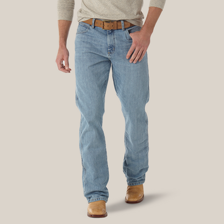 A person wearing Mens Wrangler Retro Relaxed Fit Bootcut Jeans - WRT20CR in light blue, a beige long-sleeve shirt, a brown leather belt, and tan boots stands against a plain white background.