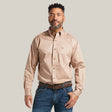 A man with short curly hair and a beard wears the Solid Twill Classic Fit Shirt Kaki - 10000505, featuring elegant embroidery. Paired with a brown belt and jeans, he stands against a plain white backdrop, exuding timeless style.