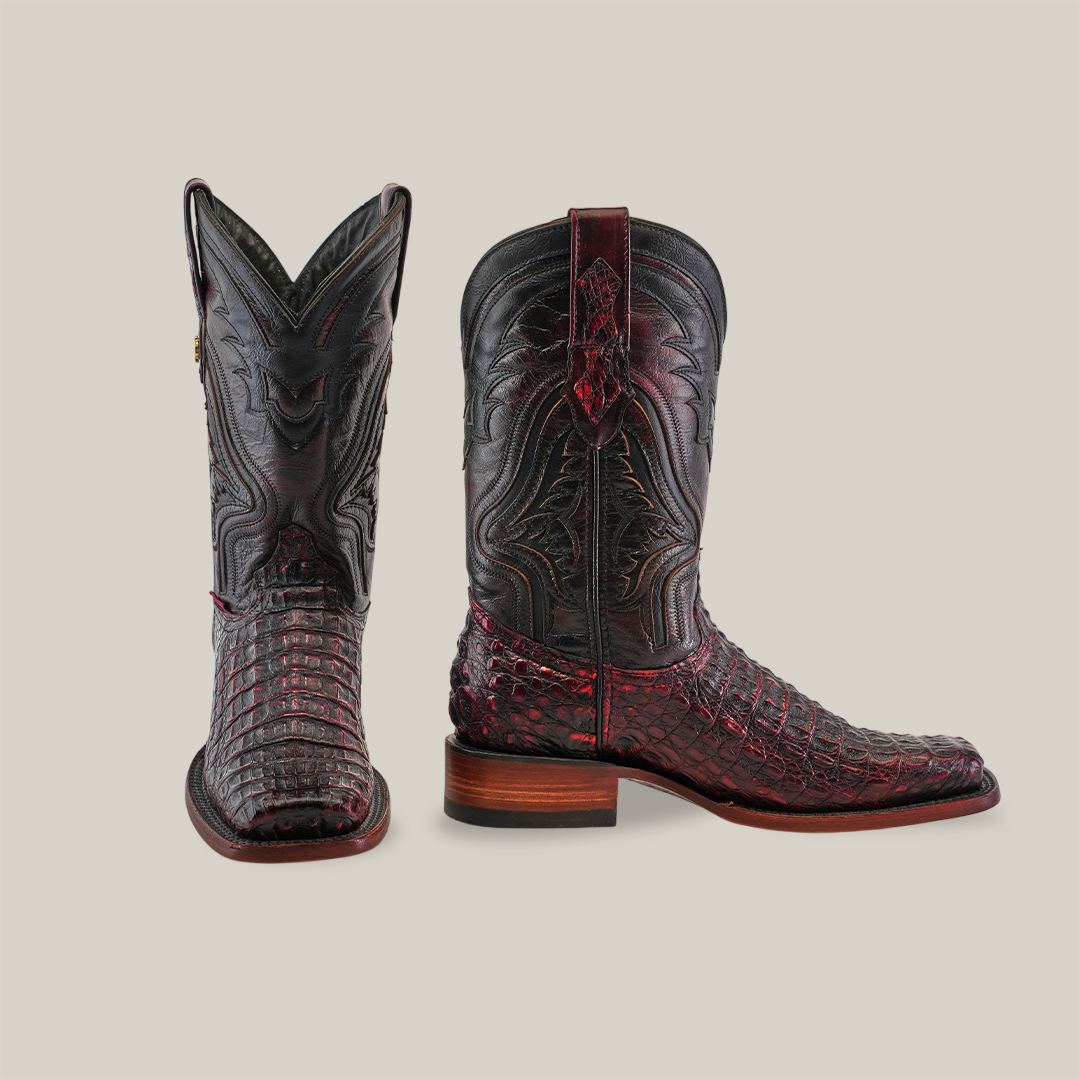 The Exotic Caiman Hornback boots in Black Cherry with a Rodeo Toe showcase one boot facing forward and the other to the side, highlighting their dark tones, intricate patterns, textures, wooden heel, and authentic caiman leather mix of smooth and scaly surfaces.