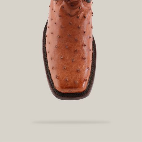 A detailed view of the Exotic Ostrich - Brandy - Rodeo Toe cowboy boot highlights its superb craftsmanship and unique bumpy ostrich leather texture. The brown boot features a rodeo toe and intricate stitching, presented against a plain white backdrop.