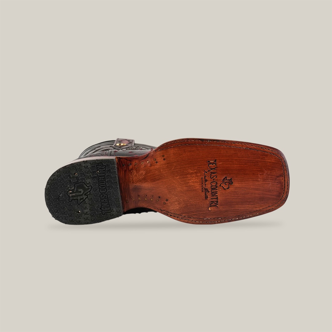 From the bottom, see a Black Cherry Exotic Ostrich boot on its side, featuring an ostrich leather sole with a logo. Its heel and external material display a rugged style and distinctive rodeo toe, all set against a plain white background that highlights its craftsmanship.