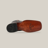 From the bottom, see a Black Cherry Exotic Ostrich boot on its side, featuring an ostrich leather sole with a logo. Its heel and external material display a rugged style and distinctive rodeo toe, all set against a plain white background that highlights its craftsmanship.