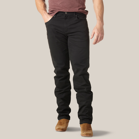 Sporting a maroon shirt, Mens Wrangler Retro Slim Fit Straight Leg Pant in black, and brown shoes, a person stands casually with hands in pockets against a minimalist background. The cropped image highlights the casual sophistication of premium denim.