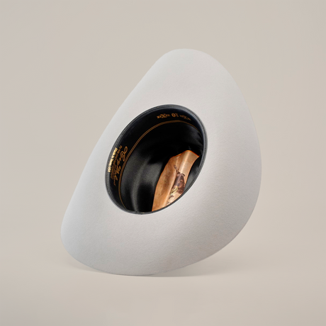 The 10X Jerarca Platinum is a large, light gray fur felt hat with a wide brim and abstract asymmetrical design. It features a black band with gold lettering and detail, standing proudly on a plain white background.