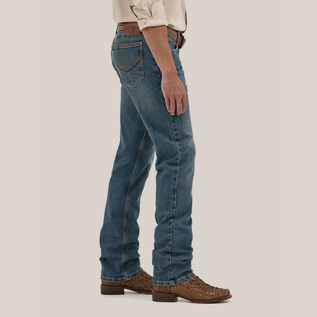 Dressed in Wrangler Mens 20X Extreme Relaxed Fit Jeans - 1044MWXMA with a beige shirt and brown woven shoes, a person stands sideways, arms at their sides. The premium denim jeans boast a classic fit with visible back pockets, while a belt peeks out against the plain light background.