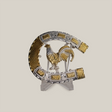 The HorseShoe Rooster is a decorative silver and gold horseshoe with ornate detailing, showcasing a golden rooster centrally. It features intricate patterns and textures, reminiscent of western designs, and is displayed on a transparent stand against a plain background.