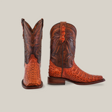 The Exotic Caiman Hornback boots in Brandy with a Rodeo Toe boast detailed stitching and textured genuine caiman leather. One boot stands upright, displaying intricate shaft patterns, while the other is angled to highlight the luxurious leather sole and textured vamp.