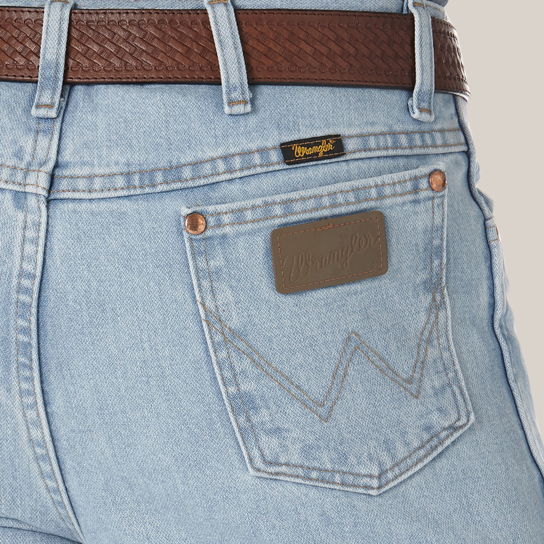 Close-up of a person in Wrangler Cowboy Cut Slim Fit Jeans - 0936GBH, light blue with a brown leather belt. The premium denim displays the classic W stitching on the back pocket with a leather Wrangler patch above it.